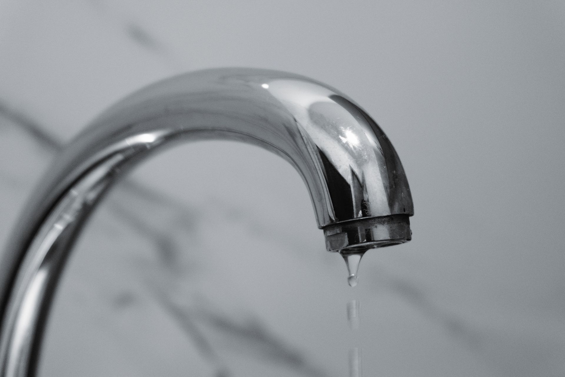A close-up shot of a modern chrome bathroom faucet with water dripping from the tip.